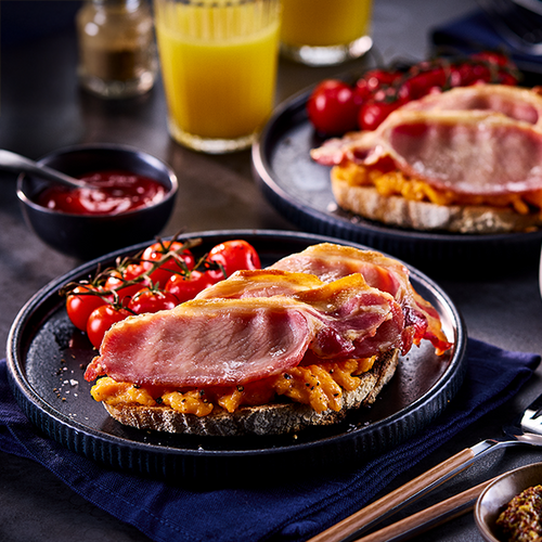 Sandwich with ham and cheese on a plate with tomatoes and a glass of juice in the background.