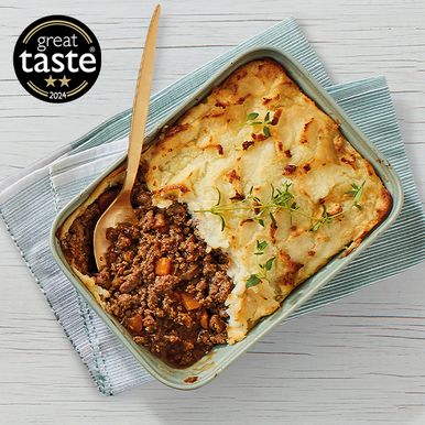 Shepherd's pie with a wooden spoon on a white surface, featuring the Great Taste award logo.