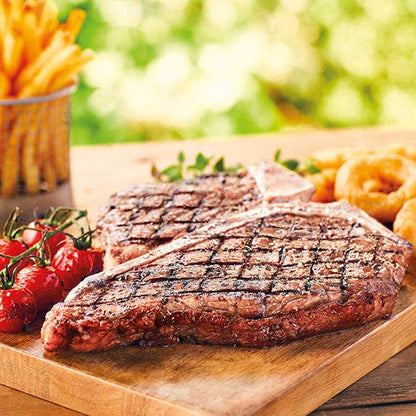 Grilled steak on a wooden cutting board with fries and vegetables in the background